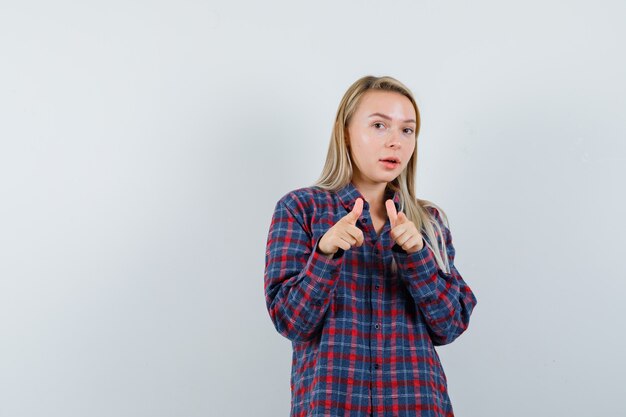 Signora bionda che indica alla macchina fotografica in camicia casual e che sembra ragionevole. vista frontale.