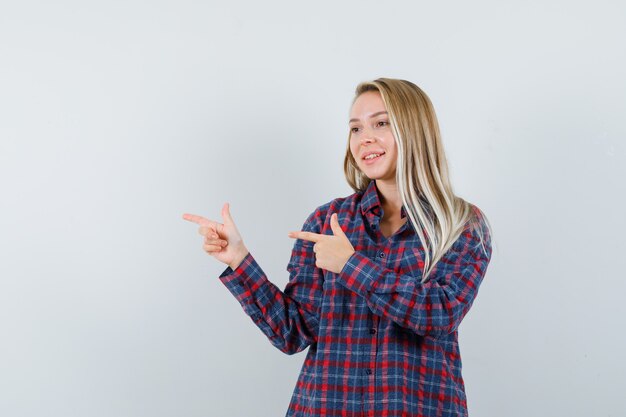 Signora bionda che indica da parte in camicia casual e sembra allegra. vista frontale.