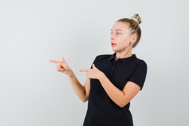 Signora bionda che indica il lato in maglietta nera e che sembra concentrata. vista frontale.