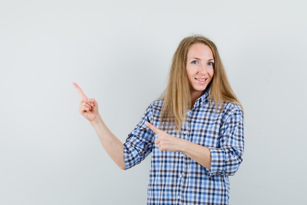 Signora bionda che indica nell'angolo in alto a sinistra in camicia e che sembra allegra.