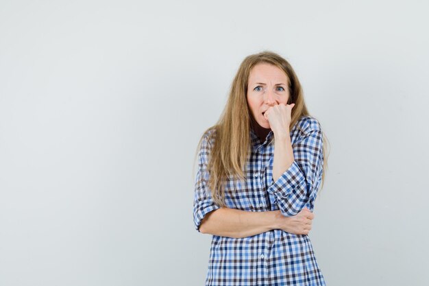 Signora bionda che morde il pugno emotivamente in camicia e sembra spaventata.