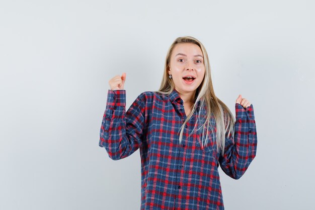 Signora bionda che mostra il gesto del vincitore in camicia casual e che sembra felice, vista frontale.