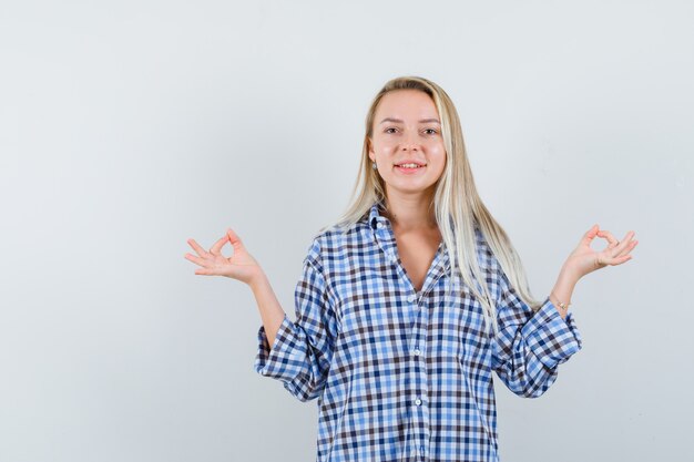 Signora bionda che mostra il gesto di meditazione in camicia a quadri e sembra gioviale