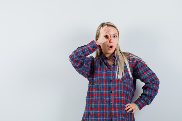 Signora bionda che mostra il gesto giusto sull'occhio in camicia casual e guardando stupito. vista frontale.