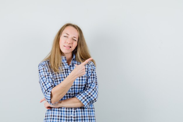 Signora bionda che punta all'angolo in alto a destra in camicia e sembra sicura,