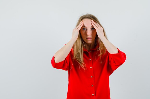 Signora bionda che si strofina la fronte in camicia rossa e sembra perplessa,