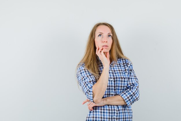 Signora bionda che tiene il mento in camicia e guardando pensieroso,