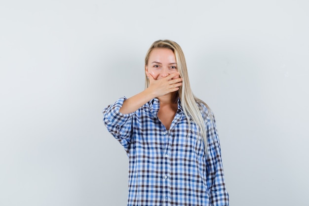 Signora bionda che tiene la mano sulla bocca in camicia controllata e che sembra felice