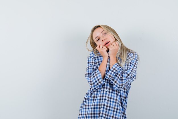 Signora bionda che tiene le mani sul mento in camicia a quadri e che sembra carina