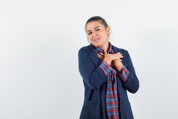 Signora bionda che tiene le mani sul petto in camicia, giacca e guardando grato, vista frontale.