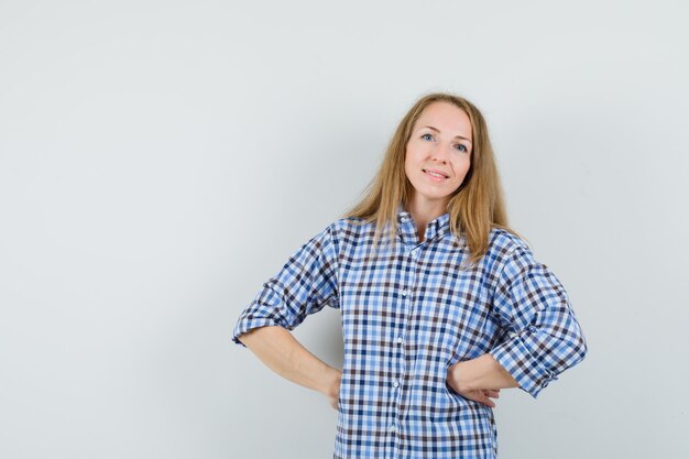 Signora bionda che tiene le mani sulla vita in camicia e guardando fiducioso,