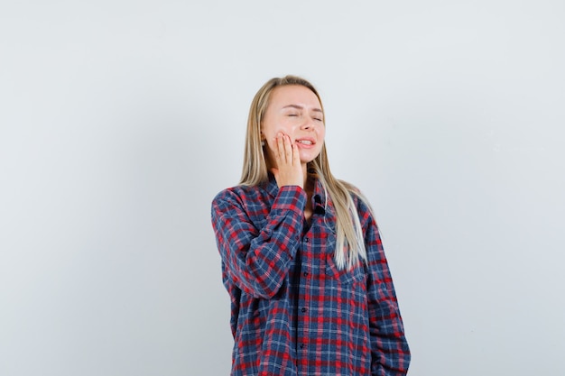 Signora bionda in camicia casual che tiene la mano sulla guancia e dall'aspetto sognante, vista frontale.