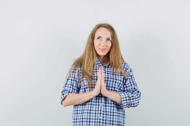 Signora bionda in camicia che mostra il gesto di namaste e sembra speranzosa,