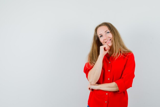 Signora bionda in camicia rossa appoggiando il mento sulla mano e guardando allegra,