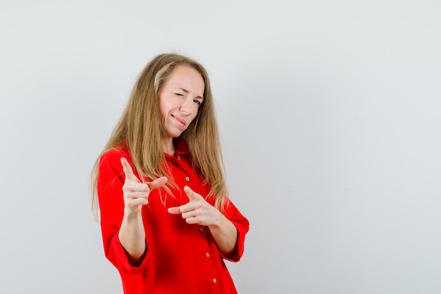 Signora bionda in camicia rossa che indica alla macchina fotografica, occhi ammiccanti e guardando fiducioso,