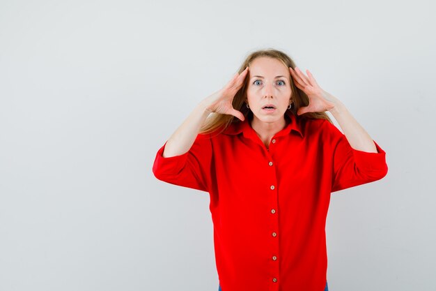 Signora bionda in camicia rossa che tengono le mani vicino alla testa e sembra scioccata,