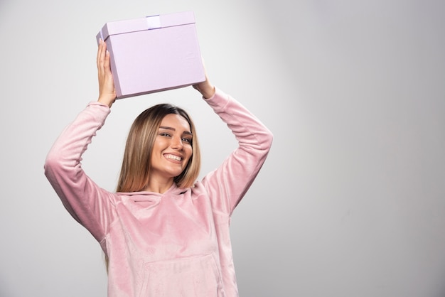 Signora bionda in felpa rosa tiene una confezione regalo sopra la sua testa e tremante.