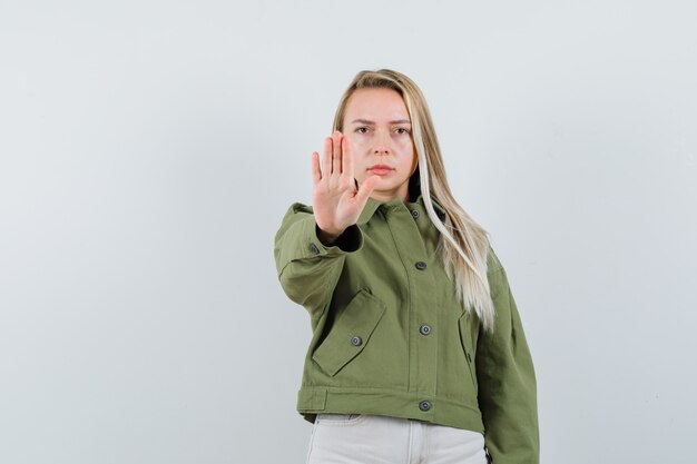 Signora bionda in giacca, pantaloni che mostrano il gesto di arresto e che sembra infastidita, vista frontale.