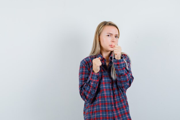 Signora bionda in piedi nella posa di lotta in camicia casual e che sembra dispettosa. vista frontale.