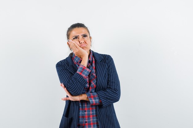 Signora bionda in piedi nella posa di pensiero in camicia, giacca e sguardo esitante, vista frontale.