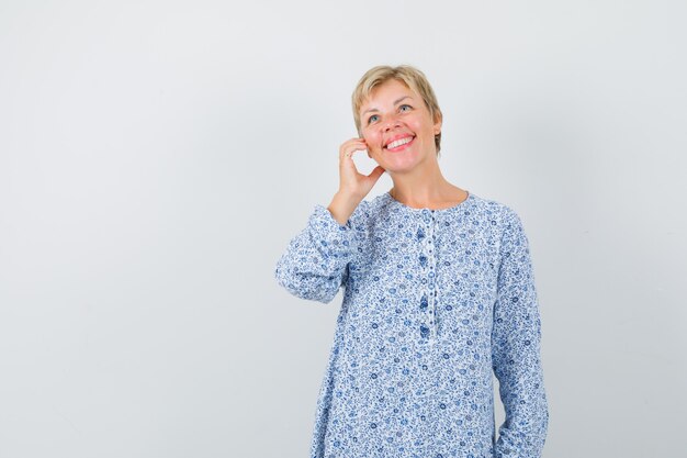 Signora bionda in posa come parlare al telefono in camicetta fantasia e guardando ottimista, vista frontale. spazio per il testo