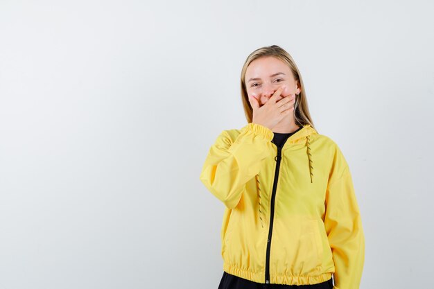 Signora bionda in tuta da ginnastica tenendo la mano sulla bocca e guardando allegro, vista frontale.