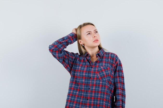 Signora bionda mantenendo la mano sulla testa in camicia casual e guardando pensieroso. vista frontale.