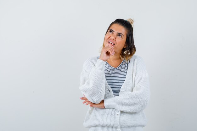 Signora carina che tiene la mano sul mento, alza lo sguardo in maglietta, cardigan e sembra speranzosa