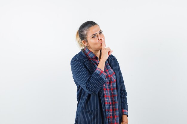 Signora che mostra gesto di silenzio in camicia, giacca e sembra sicura. vista frontale.