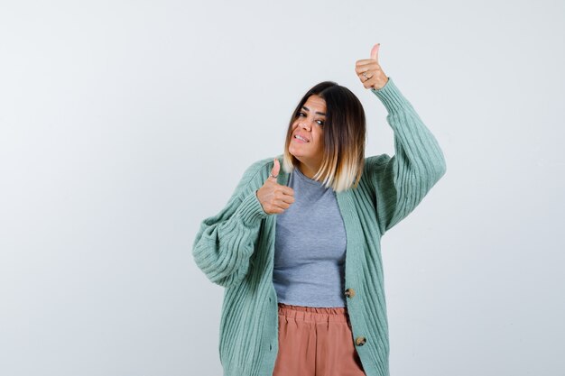 Signora che mostra i doppi pollici in su in abiti casual e sembra felice. vista frontale.