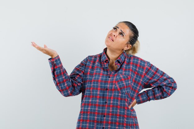 Signora che mostra qualcosa mentre cerca in camicia casual e sembra pensierosa, vista frontale.