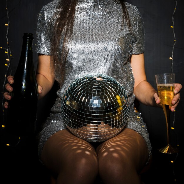 Signora con bottiglia di champagne, vetro e palla da discoteca