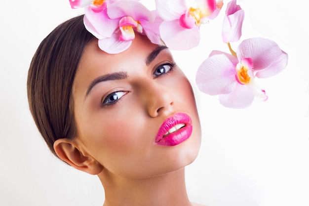 Signora con fiori di orchidea rosa, labbra grandi e trucco naturale