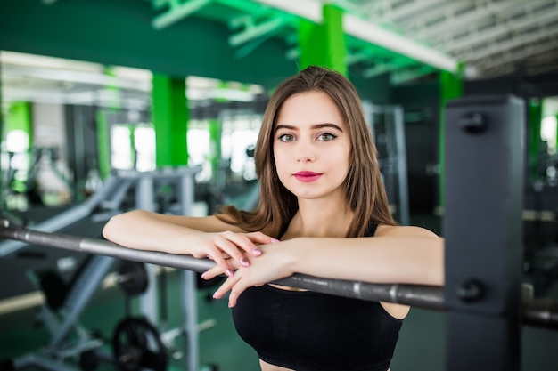 Signora con i capelli lunghi bruna e grandi occhi in posa nel moderno centro fitness vicino allo specchio in abiti sportivi corti