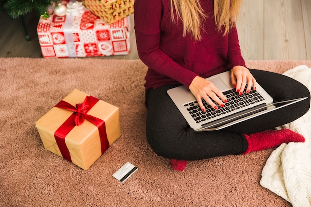 Signora con laptop vicino a carta di plastica e scatole regalo