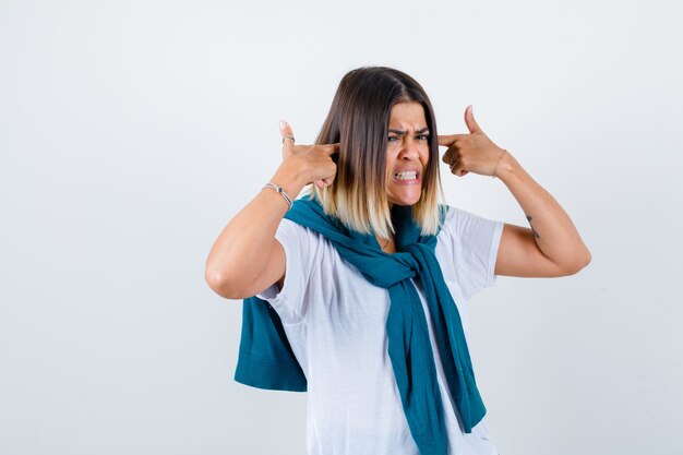 Signora con maglione legato in maglietta bianca che tappa le orecchie con le dita e sembra infastidita, vista frontale.