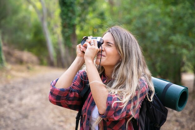 Signora concentrata riprese paesaggio e cammina con lo zaino. Turista femminile esplorando la natura, tenendo la fotocamera e scattare foto. Concetto di turismo, avventura e vacanze estive