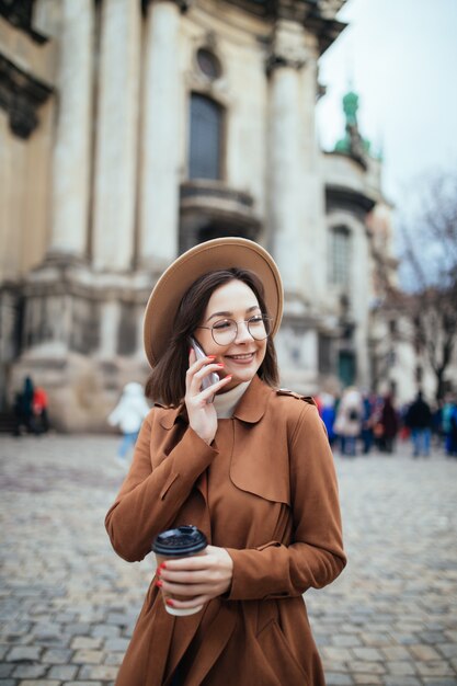 Signora dai capelli corti in cappello leggero che parla sul telefono e sui messaggi di testo sul suo telefono