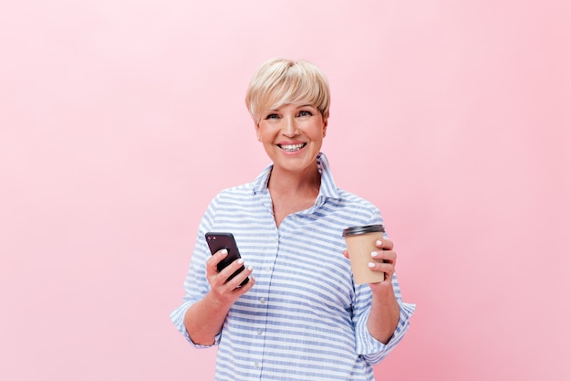Signora di buon umore posa con tazza di caffè e telefono su sfondo rosa