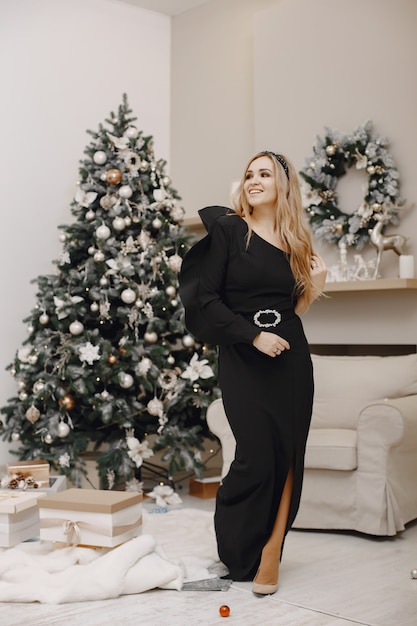 Signora elegante vicino all'albero di Natale. Donna in una stanza. Famale in un elegante abito nero.