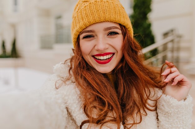 Signora europea carina che gode dell'inverno. Ragazza allegra dello zenzero in camice bianco che fa selfie all'aperto.