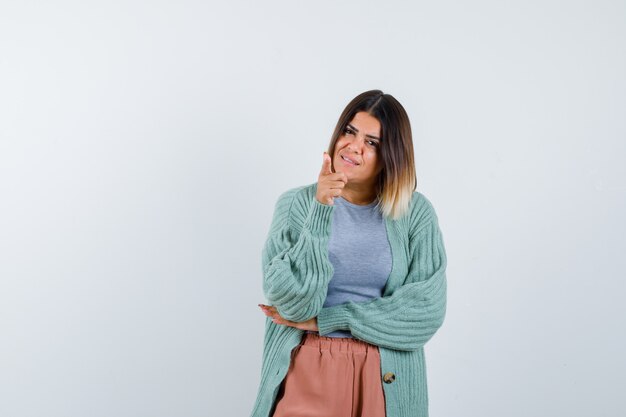 Signora in abiti casual che punta alla telecamera e che sembra esitante, vista frontale.