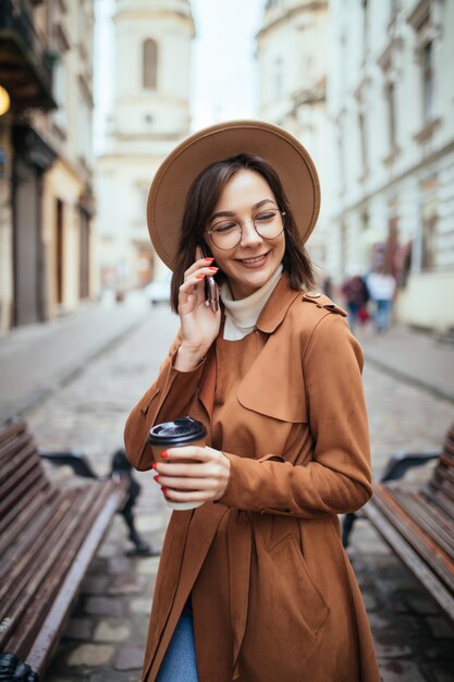 Signora in cappotto marrone che parla sul telefono cellulare che cammina all'aperto nel giorno freddo di autunno