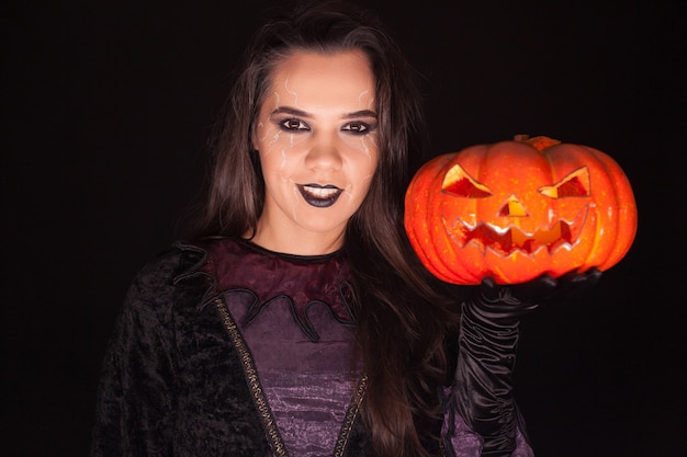 Signora in costume da strega che tiene una zucca su sfondo nero per halloween.