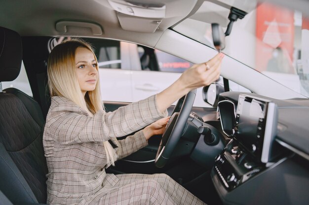 Signora in un salone di automobile. Donna che compra l'auto. Donna elegante in un abito marrone.