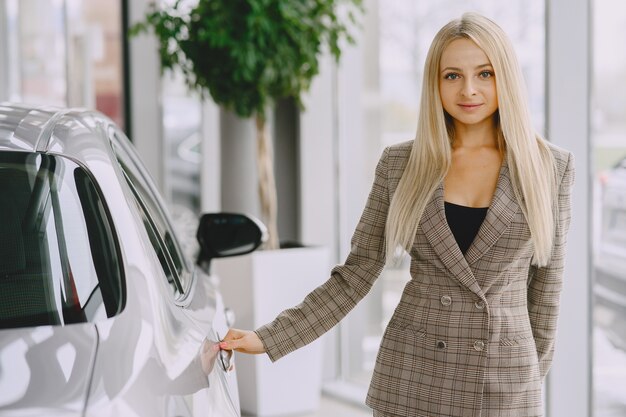 Signora in un salone di automobile. Donna che compra l'auto. Donna elegante in un abito marrone.