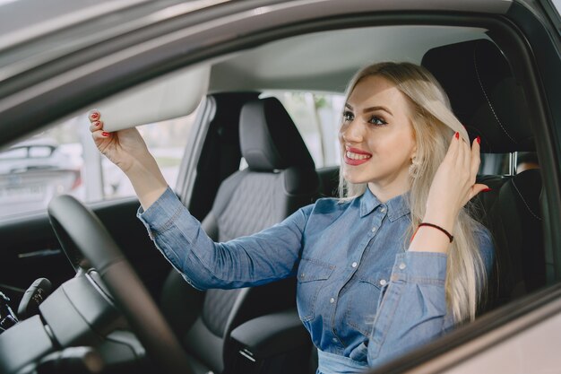 Signora in un salone di automobile. Donna che compra l'auto. Donna elegante in un vestito blu.