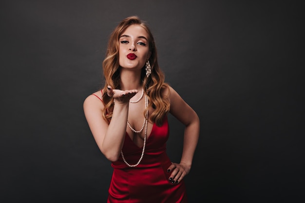 Signora in vestito rosso che soffia bacio su sfondo nero
