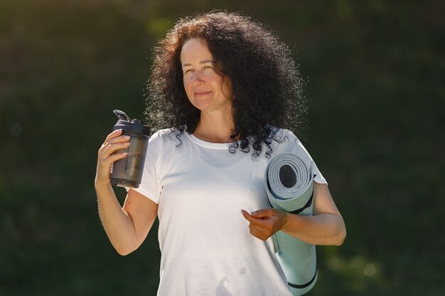 Signora matura formazione in un parco estivo. Bruna che fa yoga. Vecchia donna in abiti sportivi.