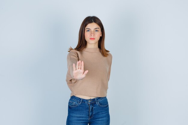 Signora meravigliosa che mostra gesto di arresto in maglione, jeans e sembra sicura. vista frontale.